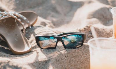 stock photo of a sandy beach with two plastic cups containing an orange drink, sunglasses, and a pair of sandals with studded straps