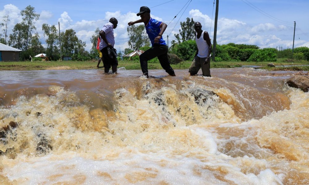 People cross a flooded portion of the road following heavy rains in Nyakach, western Kenya. Pic: AP