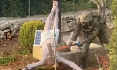 An Israeli soldier takes a sledgehammer to the face of a crucified Jesus Christ statue, which is on the ground. Taken from a BBC News report