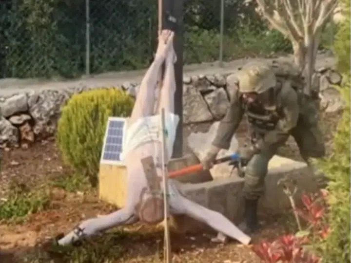 An Israeli soldier takes a sledgehammer to the face of a crucified Jesus Christ statue, which is on the ground. Taken from a BBC News report