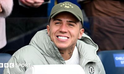 Enzo Fernandez smiling while in sat down in a Chelsea jacket