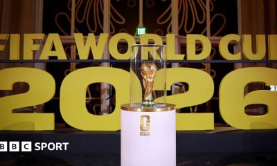The World Cup on display on a white stand prior to the draw in December in Washington with Fifa World Cup 2026 in big gold letters in the background.