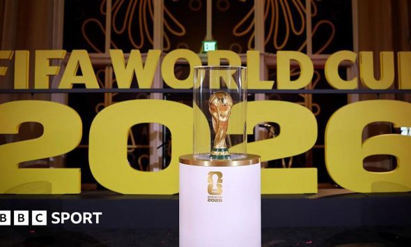 The World Cup on display on a white stand prior to the draw in December in Washington with Fifa World Cup 2026 in big gold letters in the background.