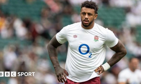 Courtney Lawes standing on the pitch with an England shirt on and his hands on his hips