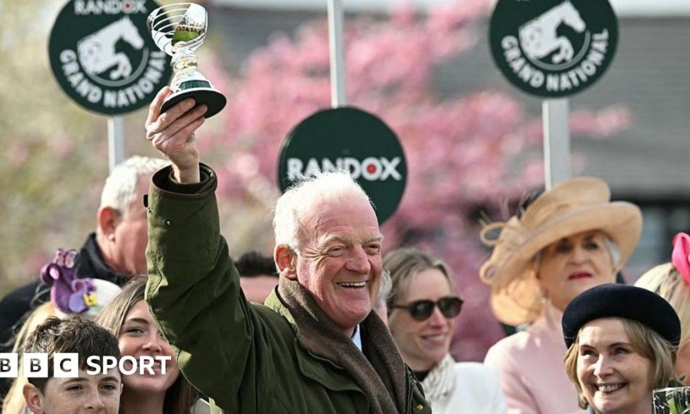 Willie Mullins smiling and holding a trophy in the air