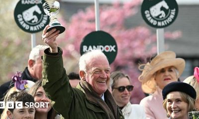 Willie Mullins smiling and holding a trophy in the air