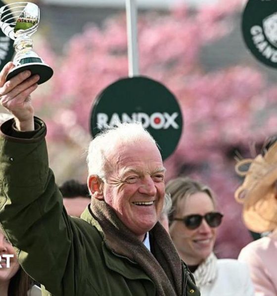Willie Mullins smiling and holding a trophy in the air