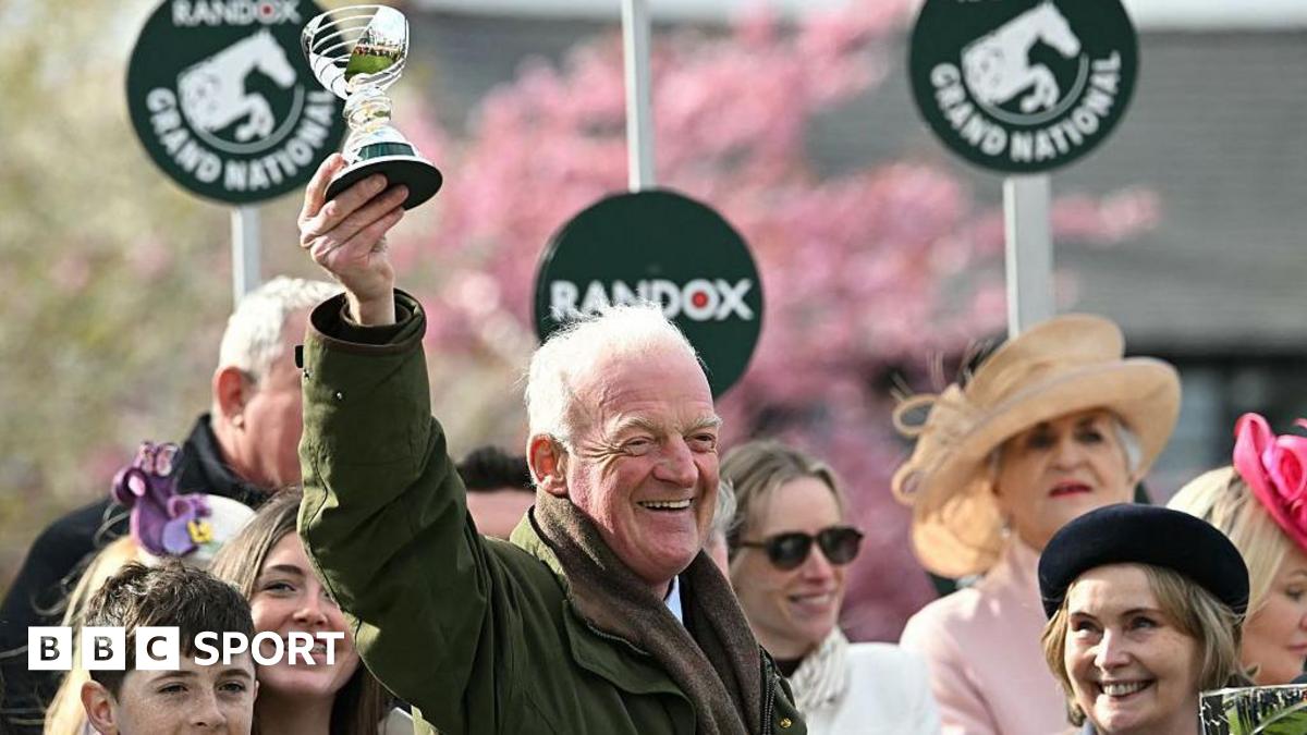 Willie Mullins smiling and holding a trophy in the air