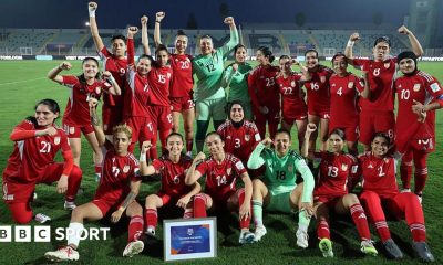 Players from the Afghan Women United team, half standing and half seated, pose for a post-match photo, smiling and with fists raised