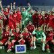 Players from the Afghan Women United team, half standing and half seated, pose for a post-match photo, smiling and with fists raised
