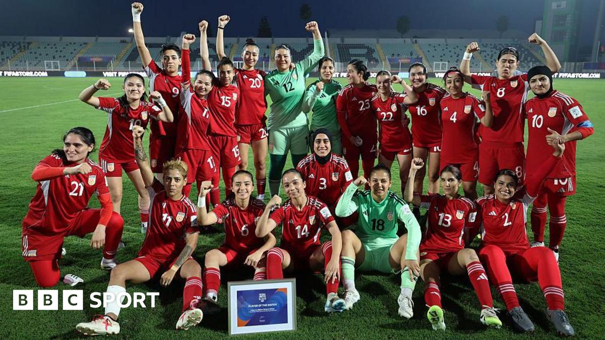 Players from the Afghan Women United team, half standing and half seated, pose for a post-match photo, smiling and with fists raised