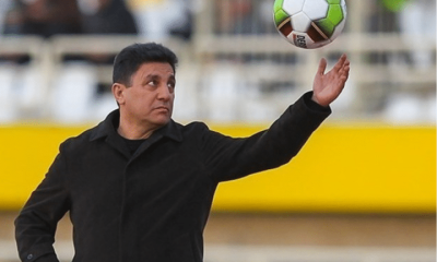 Iran national football team coach, Amir Ghalenoei, throws a football in the air with one hand while the other rests confidently in his pocket. He resembles a strong statue and stares at the ball in mid-air.