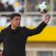 Iran national football team coach, Amir Ghalenoei, throws a football in the air with one hand while the other rests confidently in his pocket. He resembles a strong statue and stares at the ball in mid-air.