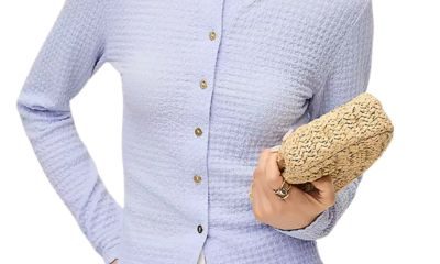 A woman wearing a light blue cardigan and white pants; she is holding a woven clutch