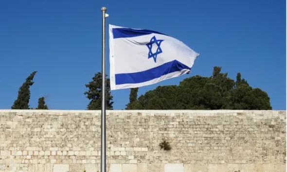 Israel's flag blows in the wind infront of a bricked wall. Israeli non-profit Shivat Zion's logo is also the Israeli flag