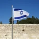 Israel's flag blows in the wind infront of a bricked wall. Israeli non-profit Shivat Zion's logo is also the Israeli flag