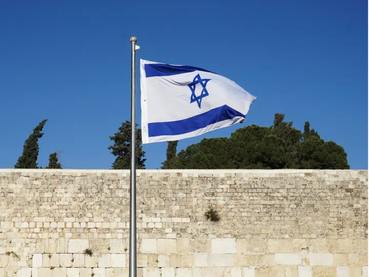 Israel's flag blows in the wind infront of a bricked wall. Israeli non-profit Shivat Zion's logo is also the Israeli flag