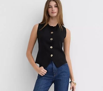 A woman wearing blue jeans and a black vest with metal buttons