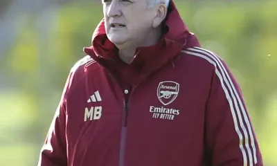 Mark Bonnick stands on the pitch wearing an Arsenal jacket with his hands in his pocket as though watching players in the distance