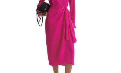 A woman wearing a pink wrap dress, gold chain necklace, and black heels. She is carrying a black handbag.