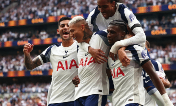 Four Tottenham Hotspur players celebrate on the pitch. One has jumped onto the other three's backs