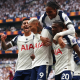 Four Tottenham Hotspur players celebrate on the pitch. One has jumped onto the other three's backs
