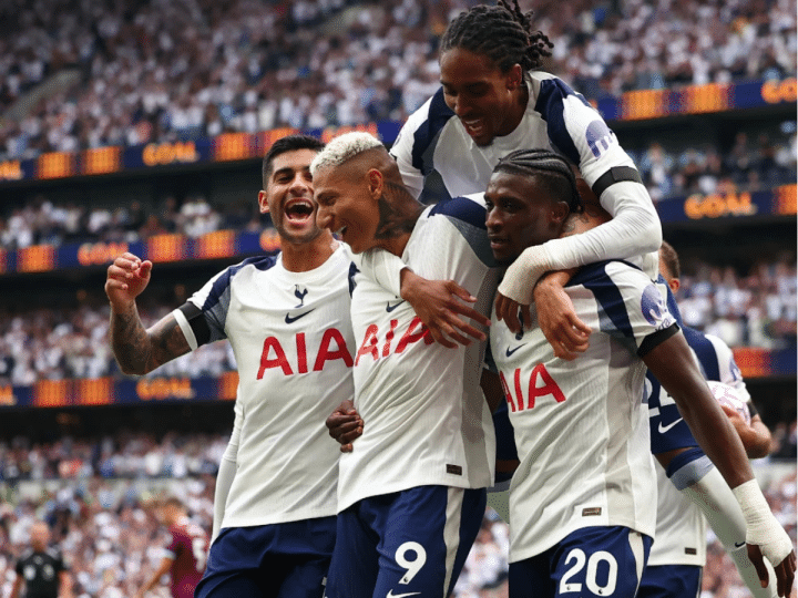 Four Tottenham Hotspur players celebrate on the pitch. One has jumped onto the other three's backs