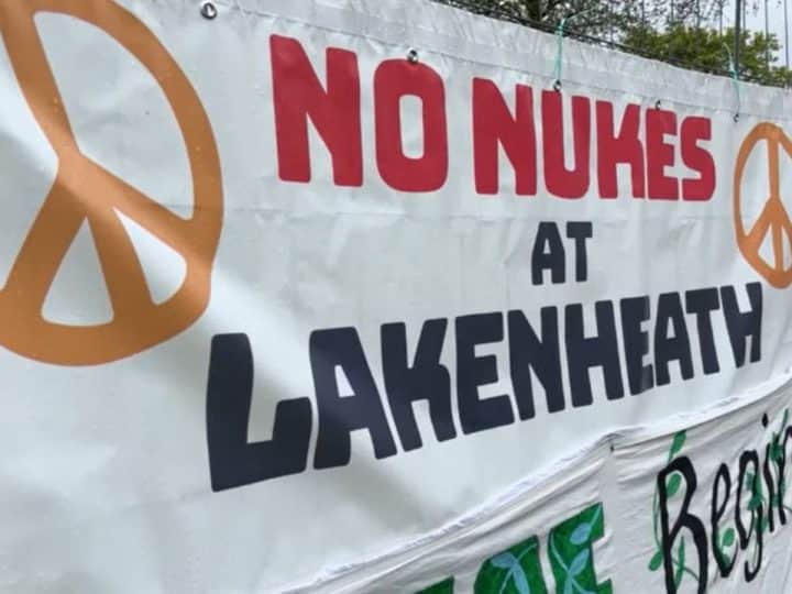 Banner with peace symbols attached to fence that reads: "No nukes at Lakenheath".