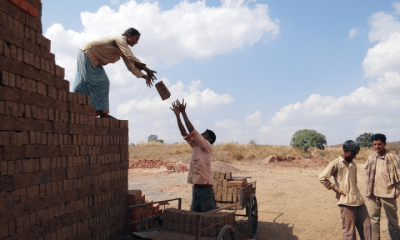 Men and women building a property in a developing country, passing each other bricks.