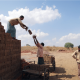 Men and women building a property in a developing country, passing each other bricks.
