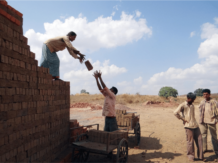 Men and women building a property in a developing country, passing each other bricks.