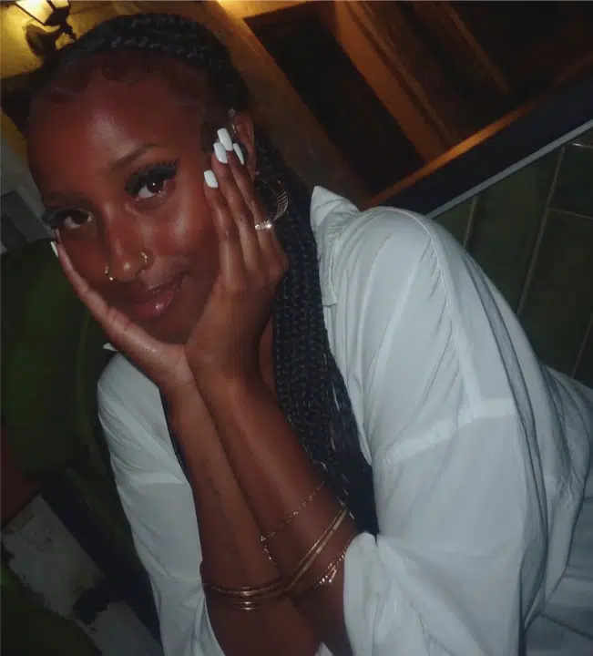 Zahwa Salah Mukhtar holds her face in her hands and smiles angelically with her mouth closed. Her finger nails are painted white and she's wearing a white blouse. You can just see her hearing aid in her left ear.