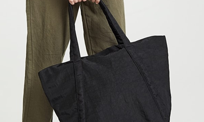 woman in olive jumpsuit holds black fabric tote bag