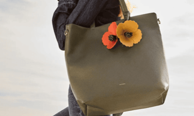 woman carries large olive green tote with orange leather poppy-shaped "charms" dangling from the handles