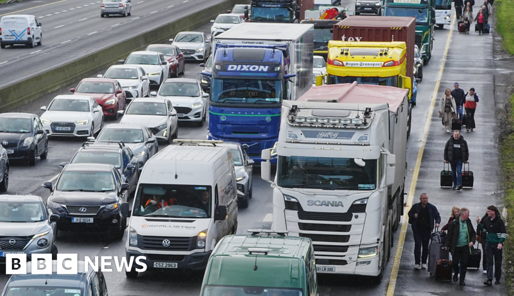 People walk with luggage past heavy traffic on Dublin's M50