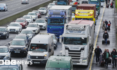 People walk with luggage past heavy traffic on Dublin's M50