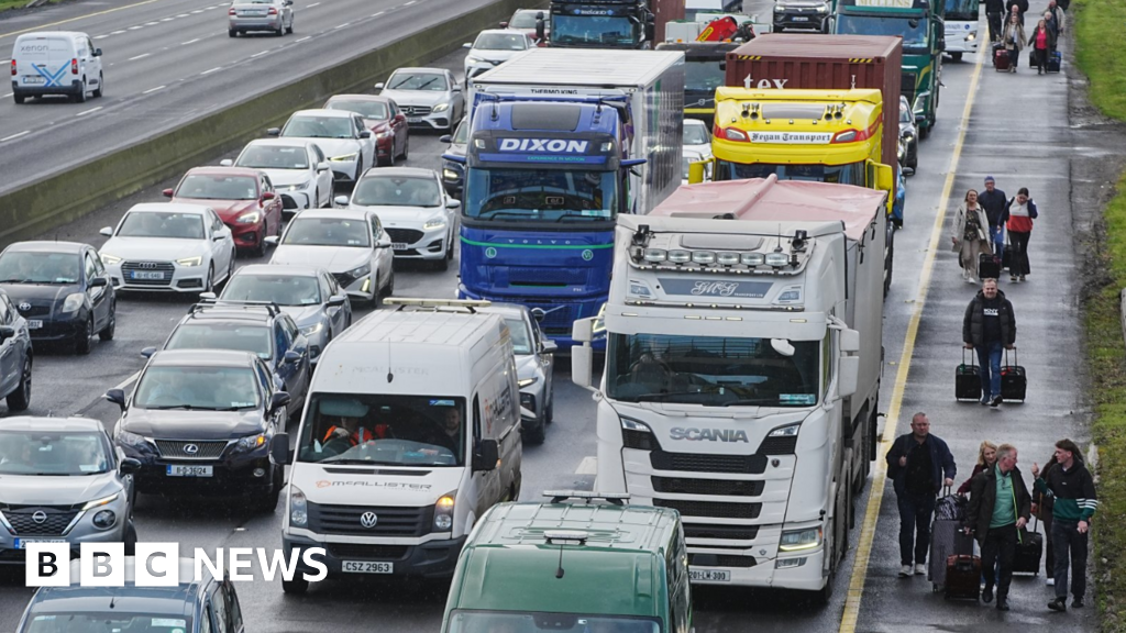 People walk with luggage past heavy traffic on Dublin's M50