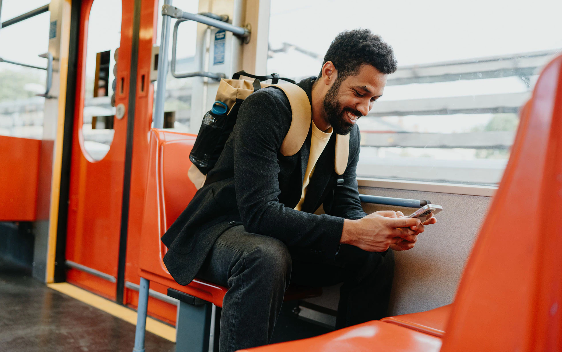 A man on a train looking at his phone and smiling