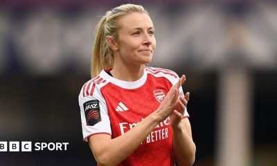 Leah Williamson, in a red Arsenal shirt with white sleeves and blonde hair tied back in a ponytail, looks in the direction of the crowd and applauds