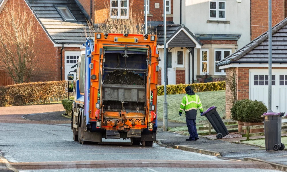 Municipal Refuse Truck and Worker in Hi-Vis Vest Collecting Residential Waste Recycling Wheelie Bins in Suburban Residential Street