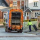 Municipal Refuse Truck and Worker in Hi-Vis Vest Collecting Residential Waste Recycling Wheelie Bins in Suburban Residential Street