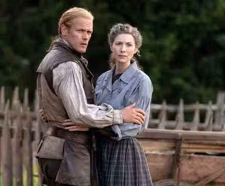 Caitriona Balfe as Claire with Sam Heughan as Jamie holding each other at the waist in Outlander Season 8