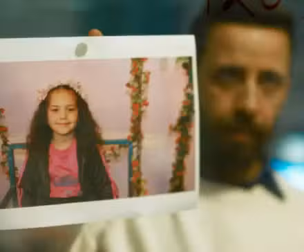 A man showing a polaroid of a young girl in The Voice of Hind Rajab