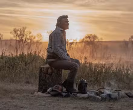 Kurt Russell as Preston Clyburn sitting beside a campfire on 'The Madison'