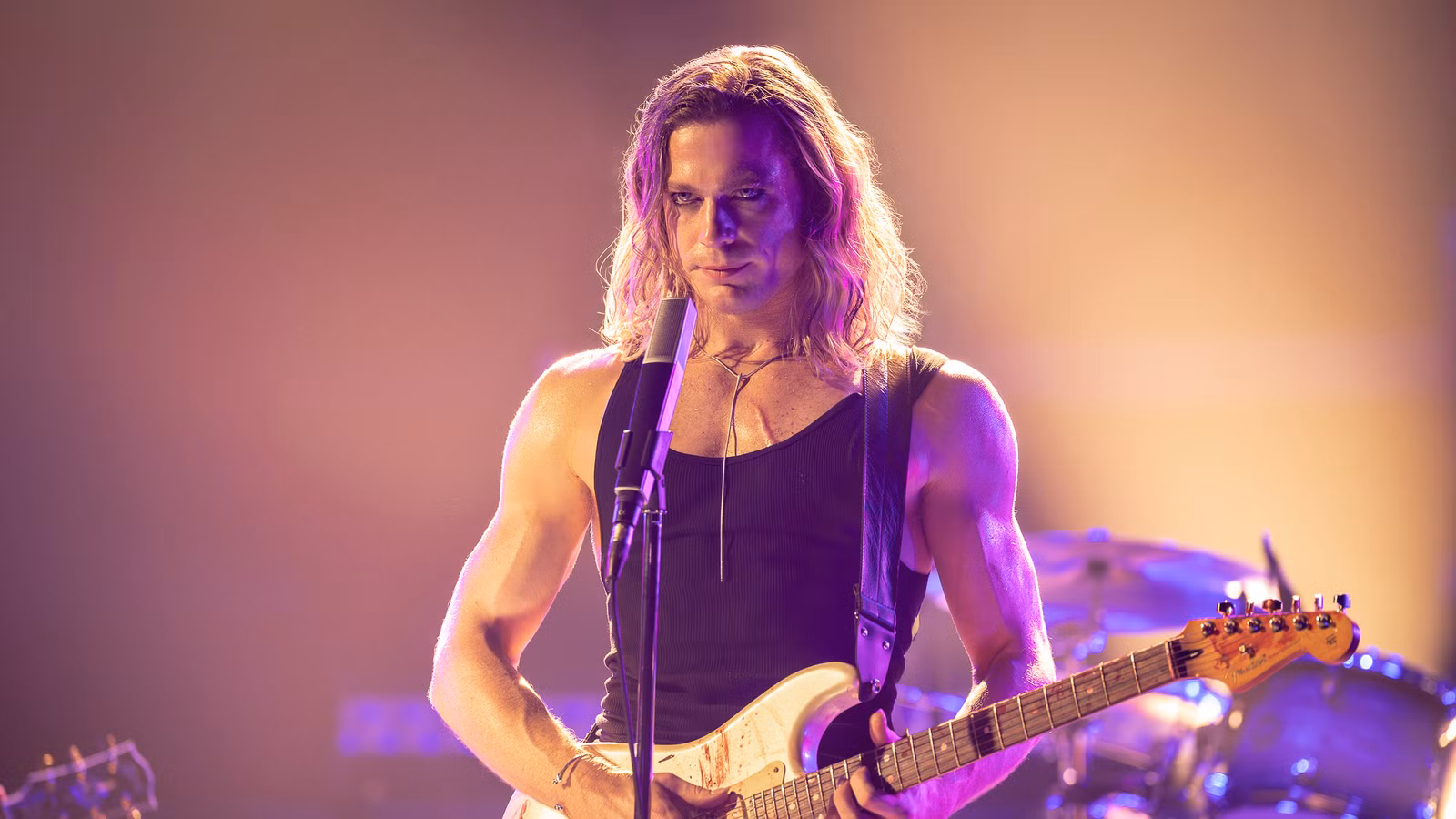 Sam Reid holding a guitar and standing in front of a microphone in The Vampire Lestat
