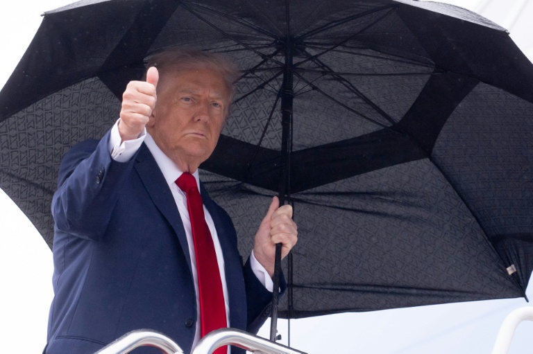 US President Donald Trump holds an umbrella as gives a thumbs up while boarding Air Force One prior to departure from Joint Base Andrews in Maryland, October 12, 2025
