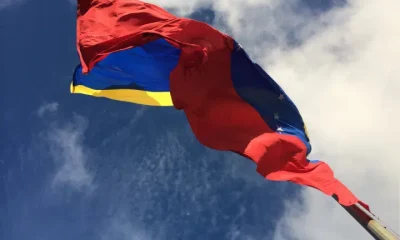 The IMF and World Bank resume dealings with Venezuela. The country's flag blows in the wind with bright blue skies above it.