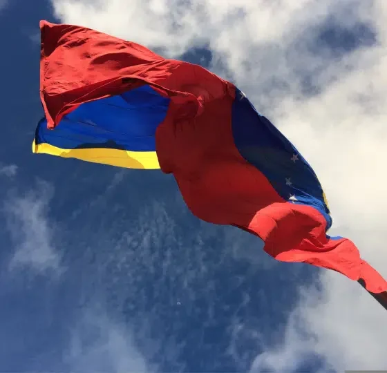 The IMF and World Bank resume dealings with Venezuela. The country's flag blows in the wind with bright blue skies above it.