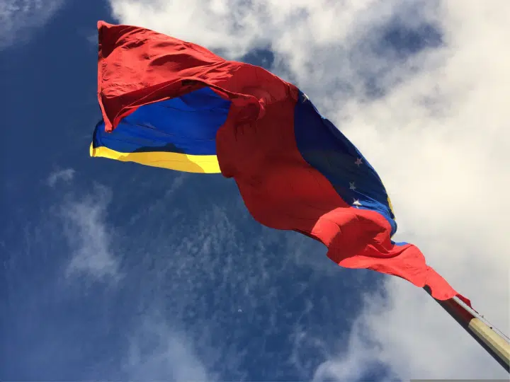 The IMF and World Bank resume dealings with Venezuela. The country's flag blows in the wind with bright blue skies above it.