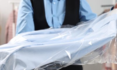 dry cleaning professional holds out a blue shirt wrapped in plastic